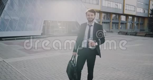 年轻的商人在开始他的工作日之前在现代办公楼前喝咖啡视频的预览图