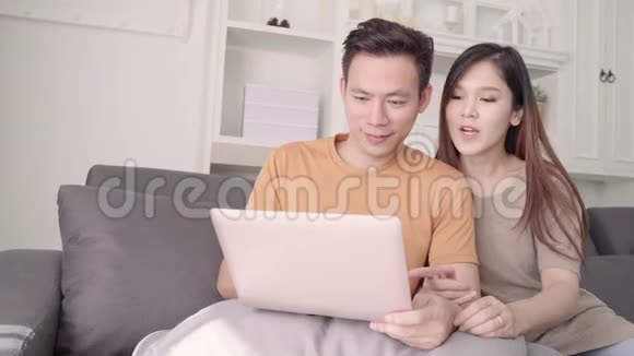 亚洲夫妇使用笔记本电脑在家里的客厅搜索网络甜蜜的夫妇享受爱情的时刻视频的预览图