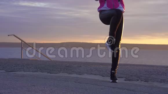慢动作一位年轻女子戴着运动帽穿着运动夹克和运动鞋在大河堤上做晨热身运动视频的预览图