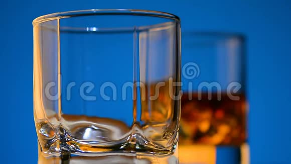 冰落在玻璃和其他玻璃上金色的饮料在蓝色的背景上全高清特写视频的预览图