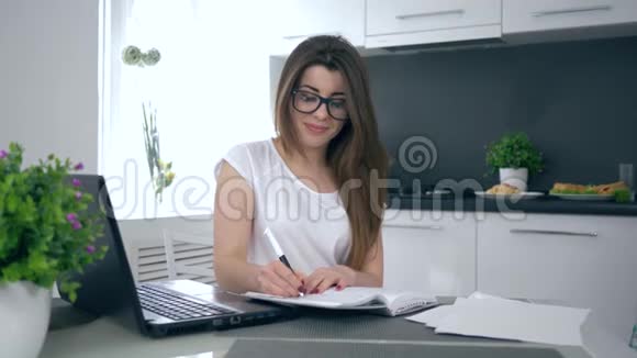 在家里成功的生意年轻的妈妈戴着眼镜在厨房的笔记本上做笔记然后快乐地拥抱儿子视频的预览图