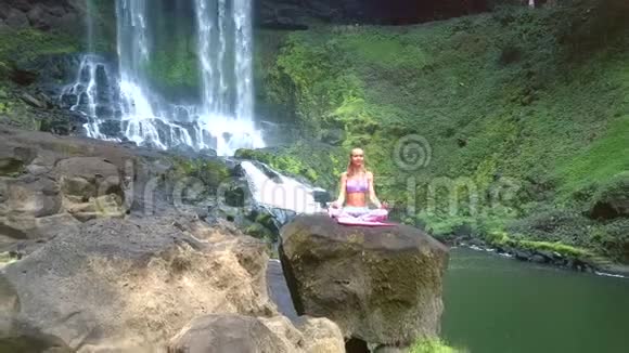 医生从坐在河边和瀑布旁的莲花姿势的女孩身上移除视频的预览图
