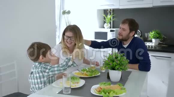 素食家庭快乐的父母带着蹒跚学步的孩子坐在厨房的桌子旁吃着美味的食物视频的预览图
