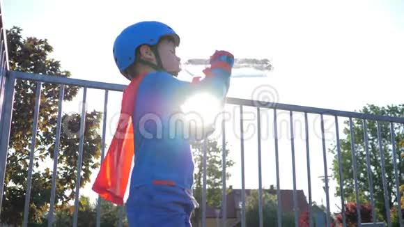 儿童饮用水男孩变成超级英雄服装与冷却饮料在塑料容器露天背光视频的预览图