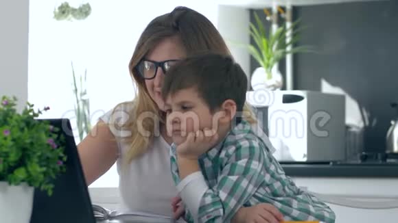 远距离学习孩子和妈妈一起做作业坐在桌子旁厨房里有笔记本电脑视频的预览图