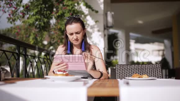 女孩在小酒馆里吃早餐在街头餐馆里用平板电脑浏览互联网视频的预览图