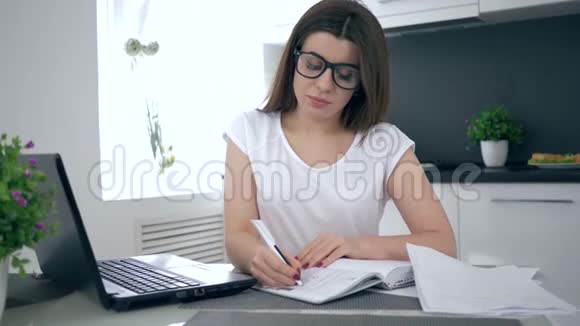 疲倦的学生坐在桌子上在笔记本上学习和写作视频的预览图