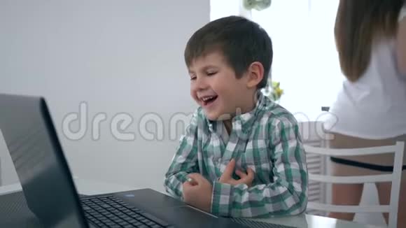 现代儿童手提电脑后坐在厨房的一张桌子旁看视频和大笑视频的预览图