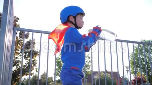 冷却饮料穿超级英雄套装的孩子手臂上有塑料瓶在户外喝矿泉水视频的预览图