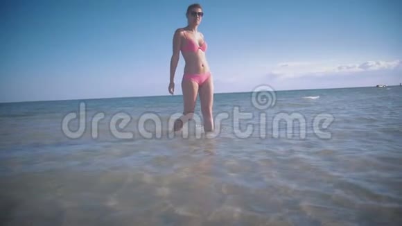 穿着粉红色泳衣和太阳镜的女孩慢慢地沿着浅海走着微笑着视频的预览图
