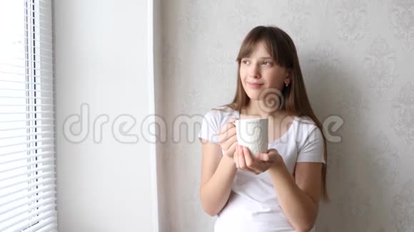 少女在窗口喝热茶微笑着视频的预览图