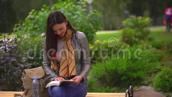 夏天年轻漂亮的女人坐在公园外面的长凳上看书4千克视频的预览图