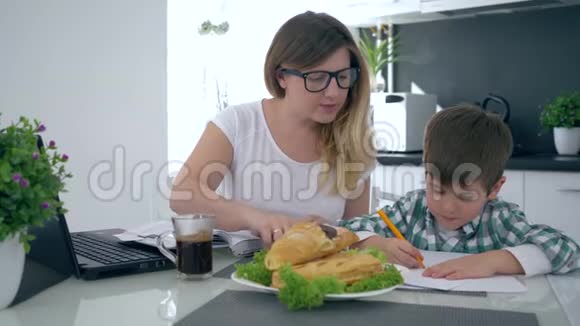 妈妈帮助儿子在早餐时坐在厨房里用彩色毡尖笔画视频的预览图