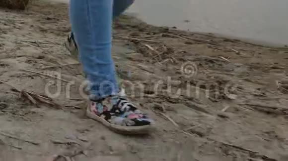 女孩穿着牛仔裤和运动鞋在海滩上散步腿特写视频的预览图