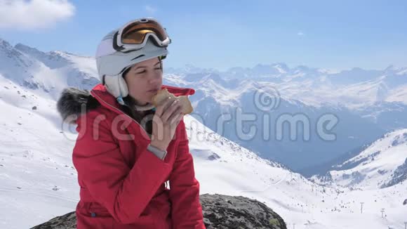 女滑雪者在高山滑雪场的石头上坐下吃三明治视频的预览图