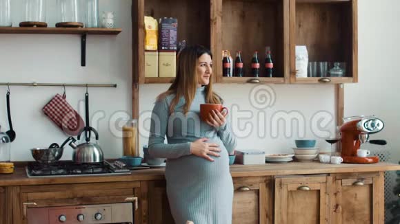 厨房里的孕妇正在喝一个红色的杯子视频的预览图