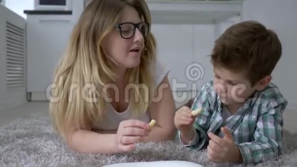 饥饿的人们和妈妈一起吃糖果的好孩子躺在家里的地板上视频的预览图