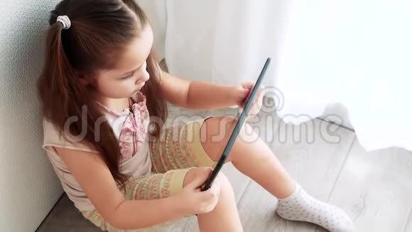 小女孩拿着电脑平板电脑坐在房间的地板上孩子学习化妆视频的预览图