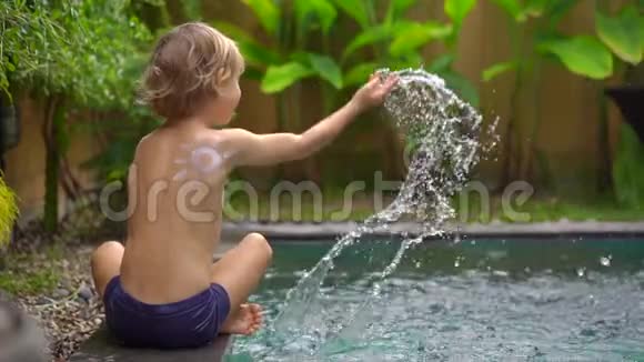 一个小男孩在游泳池里用防晒霜晒太阳动作缓慢视频的预览图