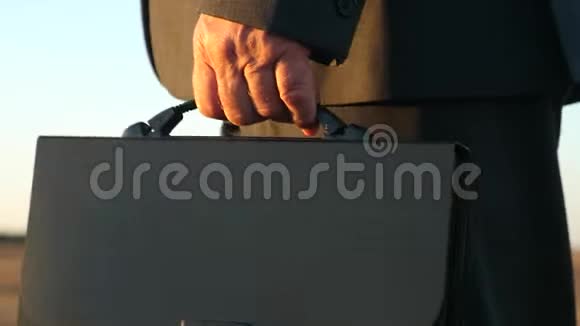 一个身穿商务服手里拿着黑色公文包的人正在公园里散步特写视频的预览图