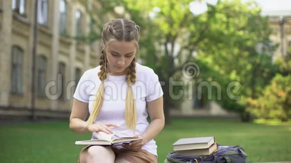 年轻女子在校园的长椅上看书准备作业教育视频的预览图