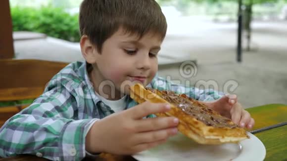饥饿有趣的小男孩在咖啡馆里吃有炼乳的圆片视频的预览图
