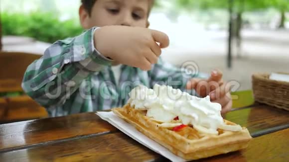 小男孩在桌旁品尝草莓和奶油的薄饼视频的预览图