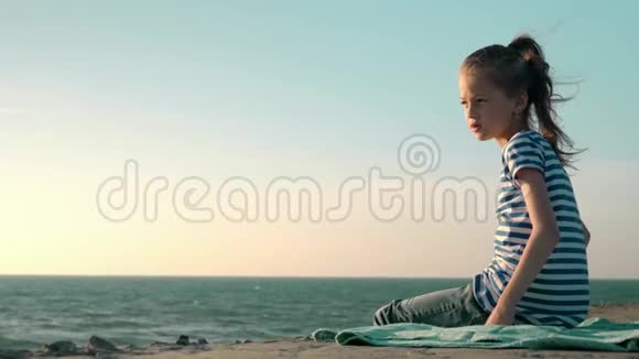 美丽的金发小女孩穿着条纹T恤坐在海滩上刮风的一天科普空间概念健康视频的预览图