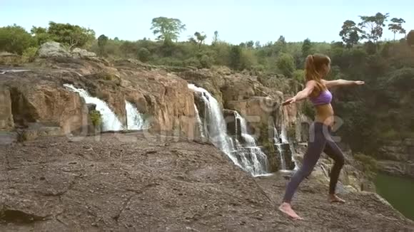 金发女孩站在瀑布附近的岩石上做瑜伽姿势视频的预览图