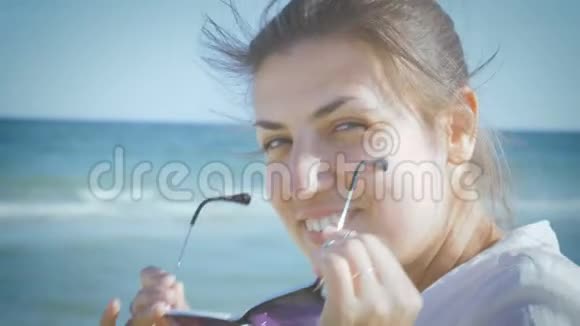 穿着白色衬衫的女孩戴上太阳镜坐在海滨微笑特写视频的预览图