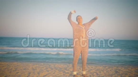 穿着睡衣伸懒腰的女孩日落时分站在海边视频的预览图