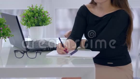 办公室工作女老板坐在办公桌旁的笔记本上写字房间里有笔记本电脑和眼镜视频的预览图