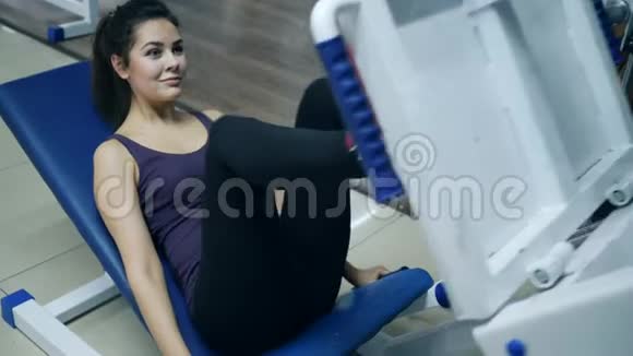 体育活动中微笑的女孩正在健身房里训练躺在腿上的压力机视频的预览图