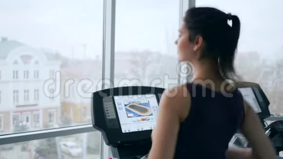 晨练快乐的女孩在跑步机上喝健身房塑料瓶中的矿泉水视频的预览图