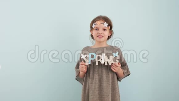 春天和欢迎春天的概念在浅蓝色薄荷背景下孩子们拿着木制装饰标志上面有视频的预览图