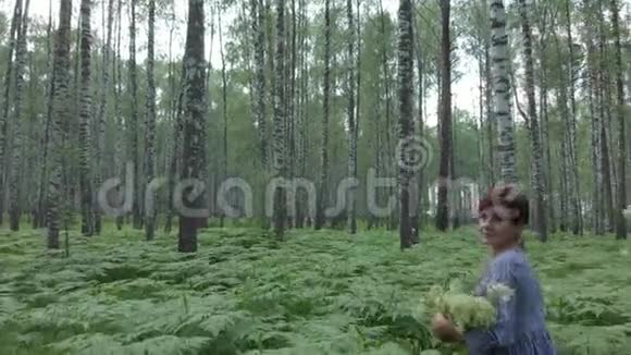 一个年轻的女人穿过一片白桦林在篮子里收集蘑菇鲜花浆果视频的预览图