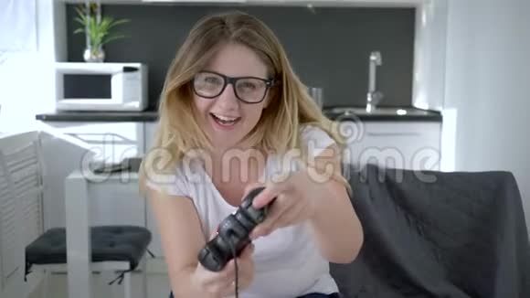 戴眼镜的女孩坐在室内沙发上玩现代游戏视频的预览图