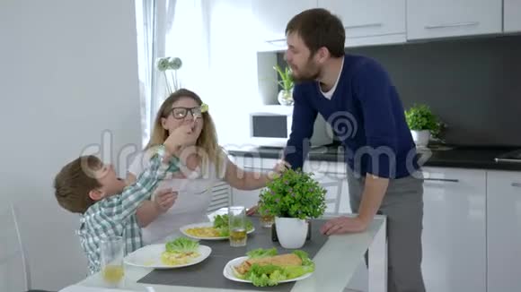 家庭午餐快乐的孩子喂爸爸美味的食物妈妈笑着坐在桌子上视频的预览图