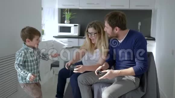 家庭娱乐父母带着孩子手里拿着游戏控制器一起玩电子游戏视频的预览图
