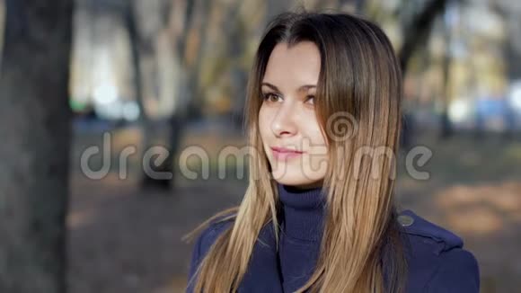 一个女人转动头慢动作的肖像4k60fps穿着外套的女孩在秋天的城市公园里散步关门视频的预览图