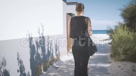 穿着黑衣服带着沙滩袋的女孩沿着通往大海的小路走从后面看视频的预览图