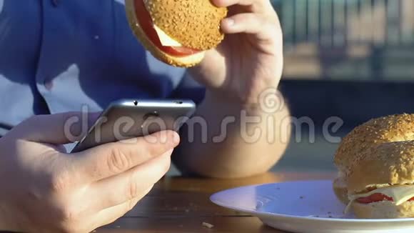 超重男人在智能手机上滚动吃快餐汉堡肥胖视频的预览图