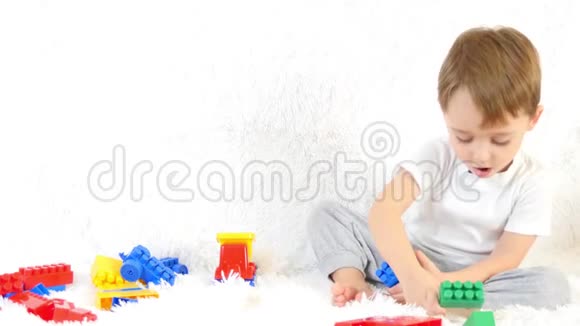 快乐的幼儿坐在沙发上在彩色的积木里玩耍坐在白色的背景上视频的预览图