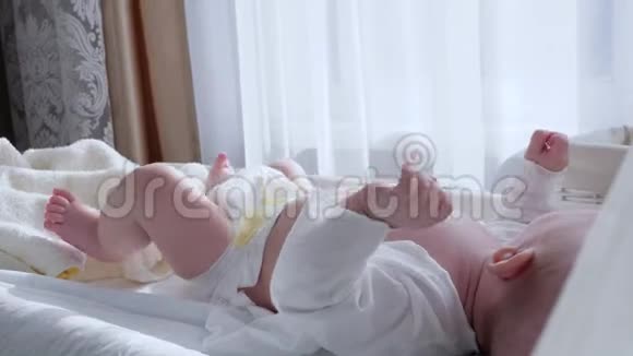 婴儿进入尿布躺在婴儿床上并拉起手脚特写视频的预览图