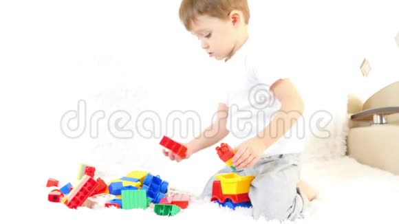 快乐的小男孩坐在沙发上玩彩色积木坐在白色的背景上视频的预览图