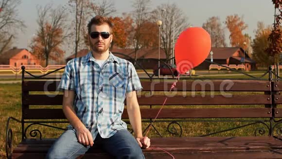 一个满脸胡须的人手里拿着一个红色气球坐在长凳上视频的预览图