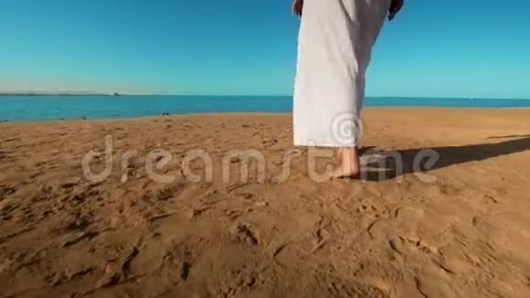 穿着白色长裙的白种人女孩在沙滩上赤脚行走的腿视频的预览图