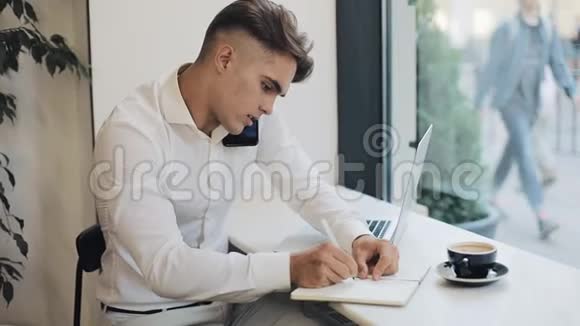 中镜头集中年轻商人在咖啡休息时打电话时在笔记本上记笔记视频的预览图