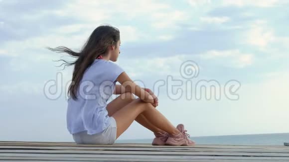 少女独自坐在海边的一座木桥上望着大海显得悲伤视频的预览图