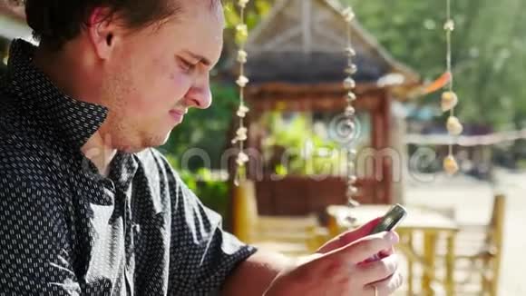 英俊的年轻悲伤男子使用智能手机坐在海滩咖啡馆3840x2160视频的预览图